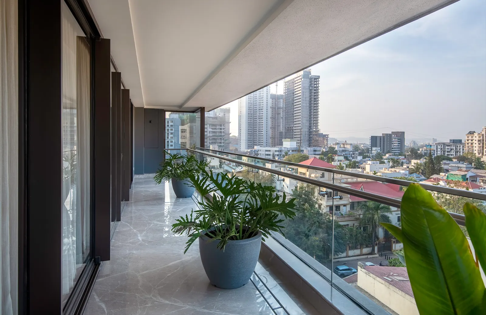 A private balcony walkway lined with planters, overlooking the city skyline