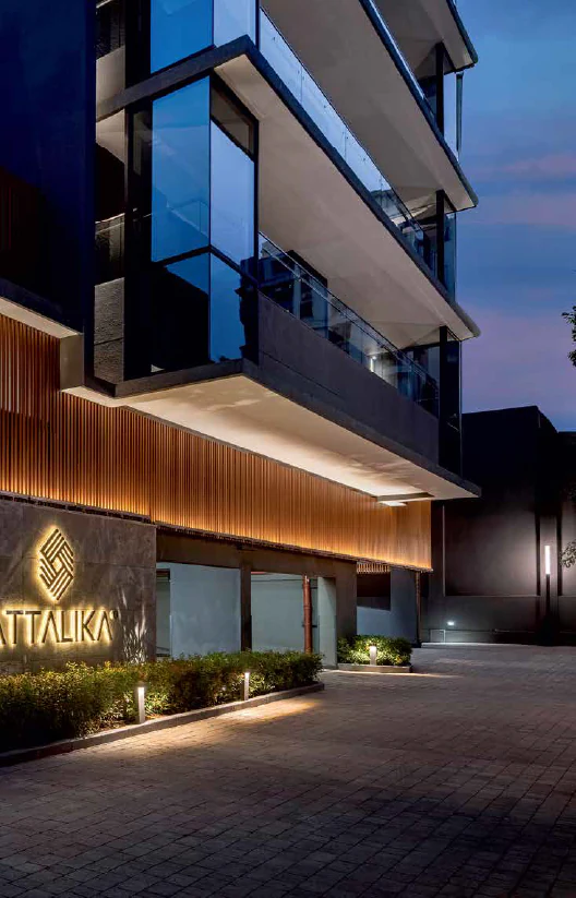 The lit entrance driveway at Attalika at dusk, the branded signage wall beside the covered parking entry